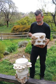 a man standing next to a white vase filled with mushrooms on top of a wooden fence