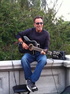 a man sitting on top of a cement wall holding a guitar