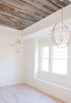 an empty room with two chandeliers hanging from the ceiling and wood flooring