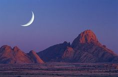 the moon is setting over some mountains in the desert with no one around it,