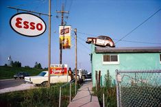 an old car sits on top of the roof of a building next to a sign that says esso