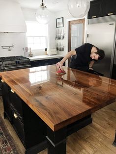 a man is sanding down on a wooden counter top in a kitchen with black cabinets and stainless steel appliances