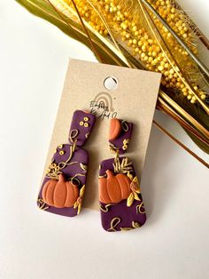 purple and orange earrings with pumpkins on them sitting next to some dried corn stalks