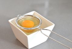 an egg in a bowl with two tongs