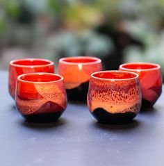 four red and black glass cups sitting on top of a gray table next to each other