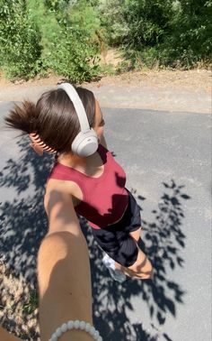 a woman with headphones on walking down the street in front of trees and bushes