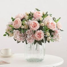 a vase filled with pink flowers sitting on top of a table next to a cup