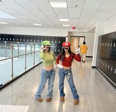 two women in jeans and baseball caps are standing on the floor with their hands up