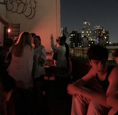 a group of people standing next to each other on a roof at night with city lights in the background