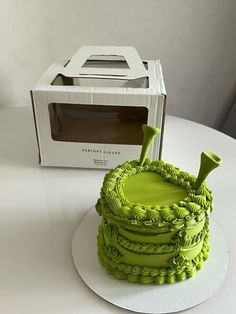 a green cake sitting on top of a white plate next to a box and microwave