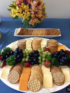 a platter of cheese, crackers and grapes on a blue table cloth