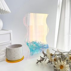 a vase with some flowers on a table next to a glass sculpture and a cup