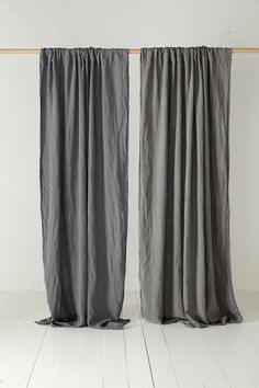 two blue curtains hanging on a wooden rail in front of a white wall and floor