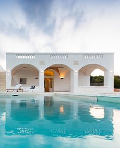 an outdoor swimming pool next to a white building with arches on the roof and windows