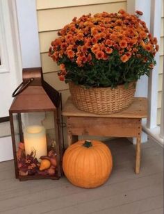 a basket full of flowers sitting next to a lantern and pumpkin on the front porch