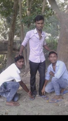 three men standing next to each other in front of trees and dirt ground with one man holding his hand out