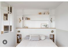 a bed with white sheets and pillows in a room next to a wall mounted bookshelf