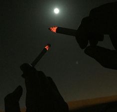 two people holding lit matches in their hands with the moon in the background at night