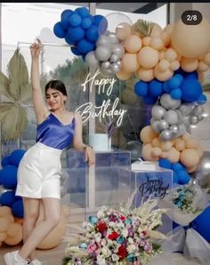 a woman is posing in front of a birthday cake with balloons and flowers on it