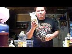 a man standing in front of a counter holding a bottle and paper towel over his mouth