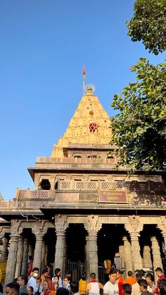 many people are standing in front of a building with an ornate roof and pillars on it