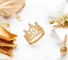 a gold ring with a crown on it next to flowers and other jewelry items,