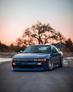 a blue sports car parked on the side of a road at sunset with trees in the background