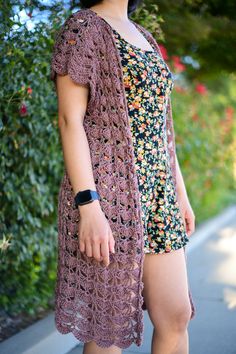 a woman standing next to a bush with her legs crossed