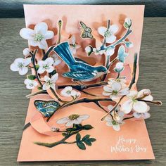 a blue bird sitting on top of a tree branch with white flowers in it's beak