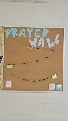 a bulletin board that says prayer wall with notes attached to it and string lights hanging from the ceiling