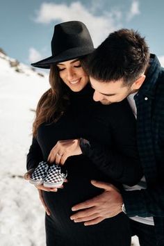 a pregnant couple cuddles in the snow while holding each other's belly