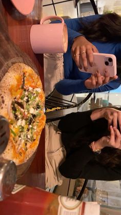 a woman taking a selfie with her cell phone while sitting in front of a pizza