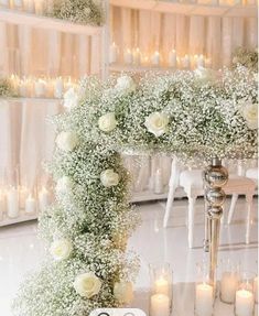 a wedding arch decorated with white flowers and baby's breath is surrounded by candles