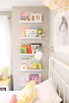 a white bed topped with lots of books next to a wall mounted shelf filled with children's books