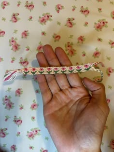 a hand holding an object in front of a floral wallpaper