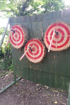 three red and white bulls eye target on a green wooden fence with trees in the background