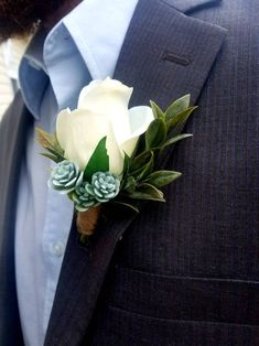 a boutonniere with white roses and succulents is worn on a man's suit