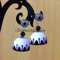 two white and black earrings hanging from a metal hook on a wooden surface with an ornamental design