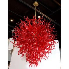 a red sculpture hanging from the ceiling in front of a white wall and light fixture