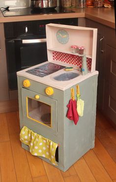 a toy stove and oven in the middle of a wooden floored kitchen with cabinets