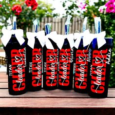 six bottles are lined up on a wooden table with flowers in the backgroud