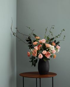 a black vase filled with pink and white flowers on top of a small wooden table