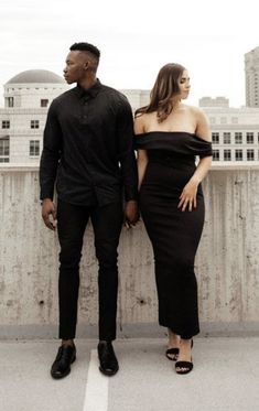 a man and woman standing next to each other on top of a roof in front of tall buildings