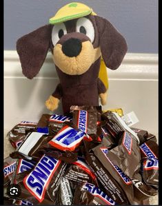 a stuffed dog sitting on top of a pile of chocolate candy bar wrapper candies