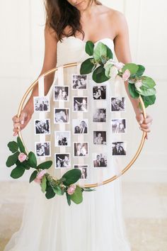 a woman in a white dress holding a circular frame with photos and greenery on it