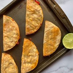 four quesadillas sitting on top of a pan with lime wedges next to them