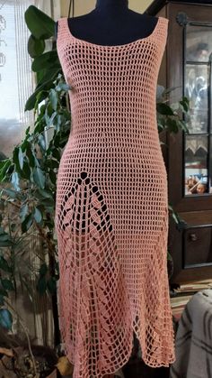 a pink crocheted dress on a mannequin next to a potted plant