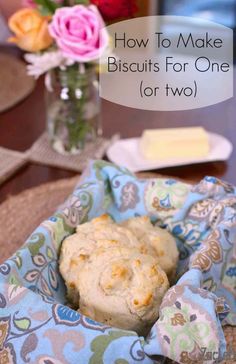 some biscuits are sitting in a basket on a table with flowers and a glass vase