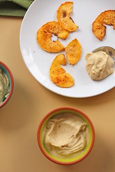 some food is on a white plate and two bowls are next to it with dip