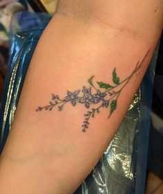 a woman's arm with purple flowers and green leaves on the left side of her arm